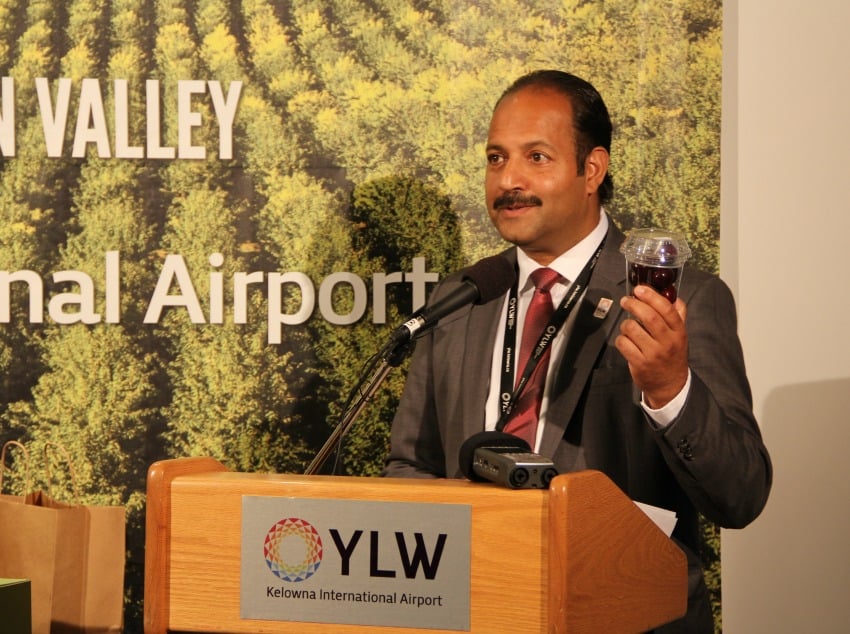<who> Photo Credit: KelownaNow. </who> Airport director Sam Samaddar showing off the plane-ready produce. 