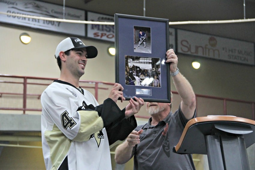 <who> Photo Credit: KelownaNow.com </who> West Kelowna mayor Doug Findlater passes a framed picture of Justin Schultz to the Kelowna-born hockey player.