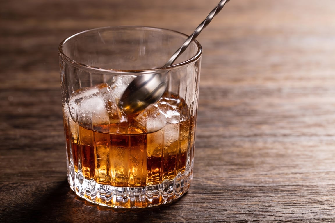 Stirring a peach bourbon cocktail with a bar spoon