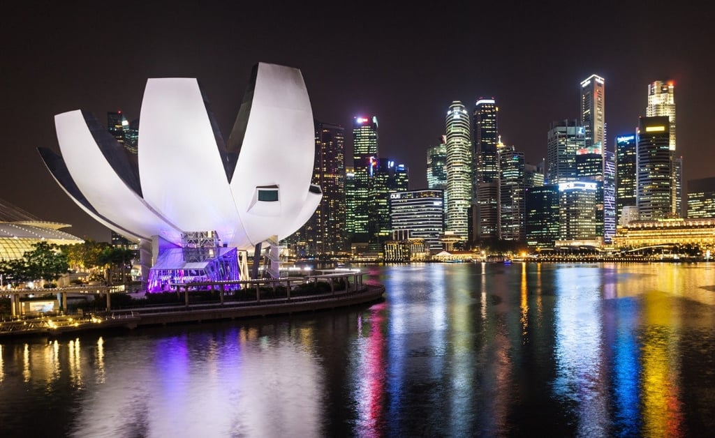 ArtScience Museum lit up at night with reflections on Marina Bay and Singapore’s skyline glowing in the background.
