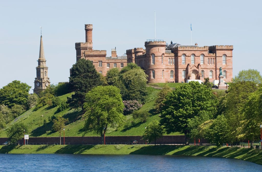 Inverness Castle, red sandstone fortress on a grassy hilltop beside the River Ness, with church spire to the left.