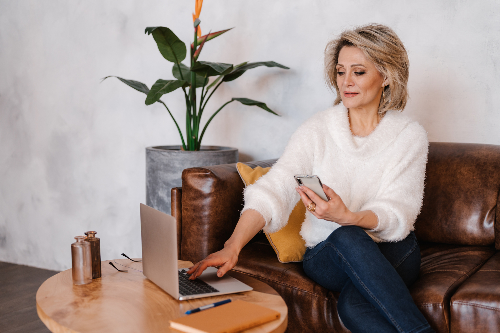 Woman seated with a smartphone and laptop nearby.