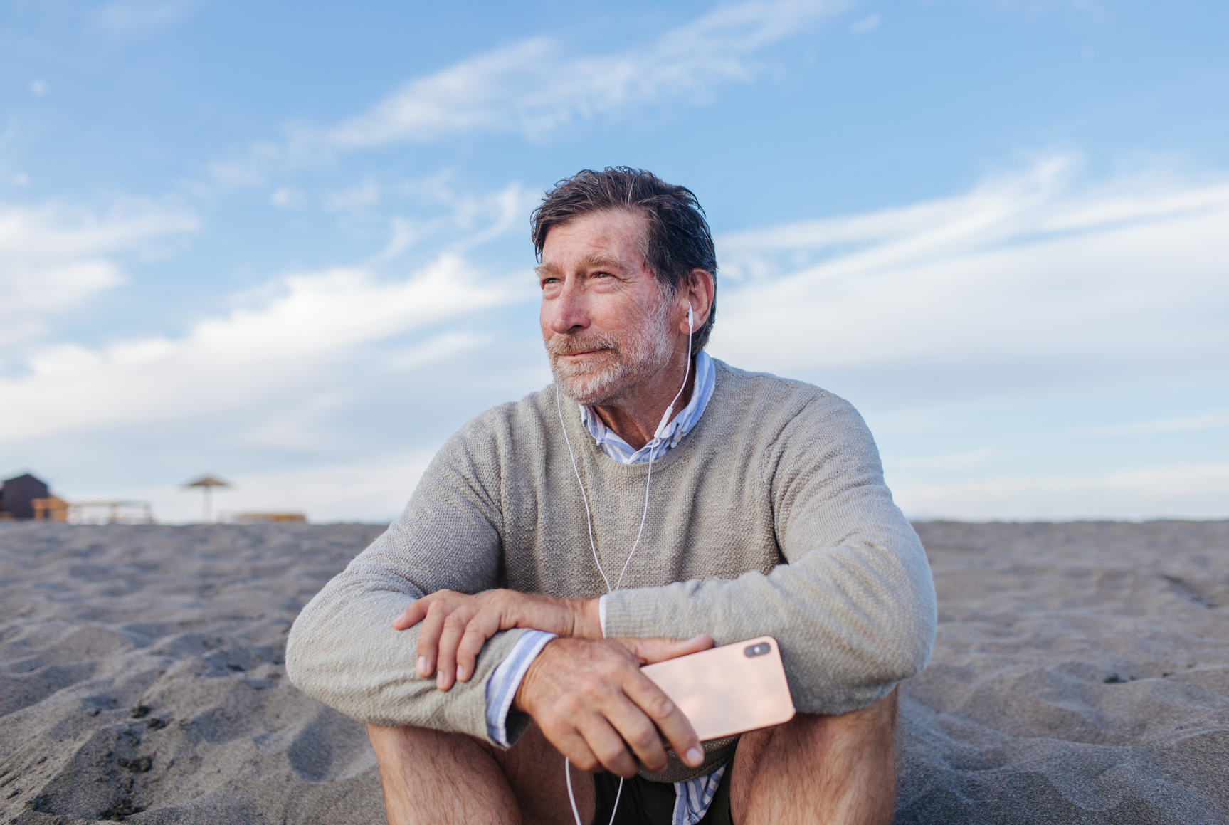 Person on a beach with headphones, holding a phone.