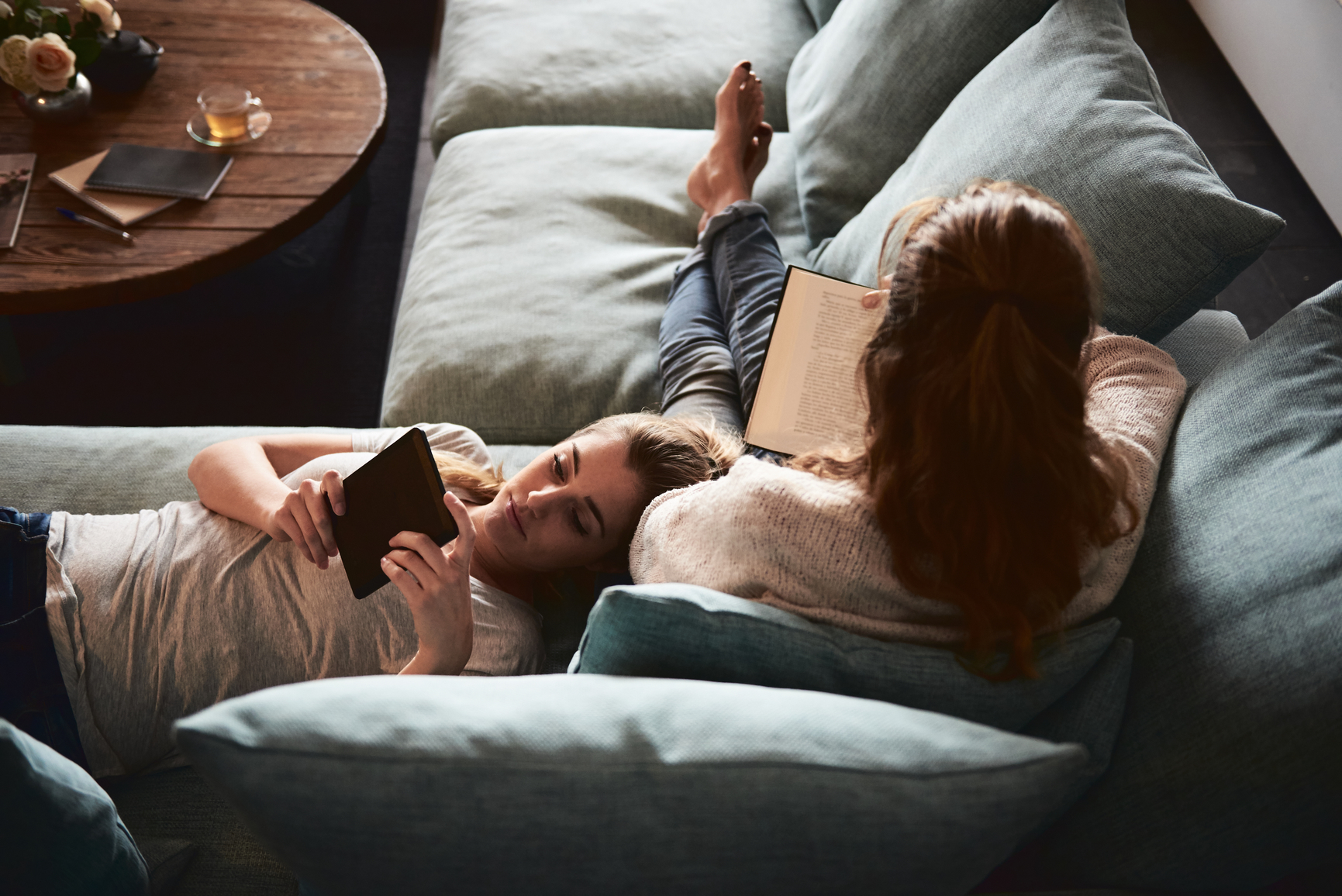 Two people reading on a couch, one with an e‑reader and one with a book.