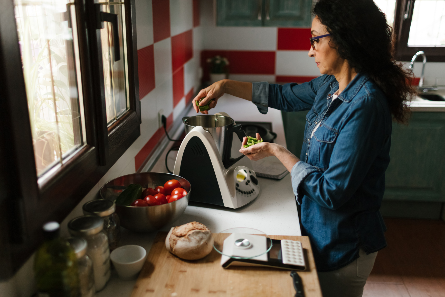 Woman adding chopped greens to a kitchen appliance.