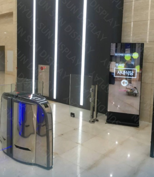 Freestanding portrait kiosk in an office lobby beside speed gates