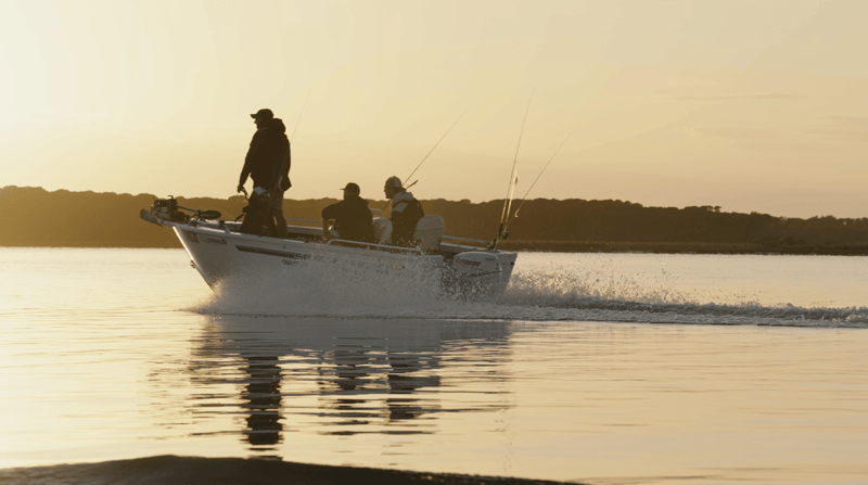 A boat of anglers cutting across glassy water at sunrise, rods up