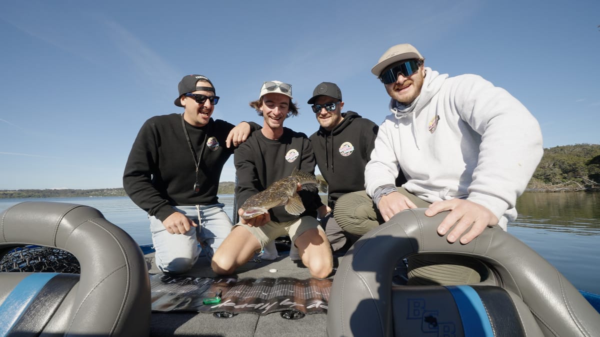 Four teammates laughing on the back deck, flathead held over the brag mat