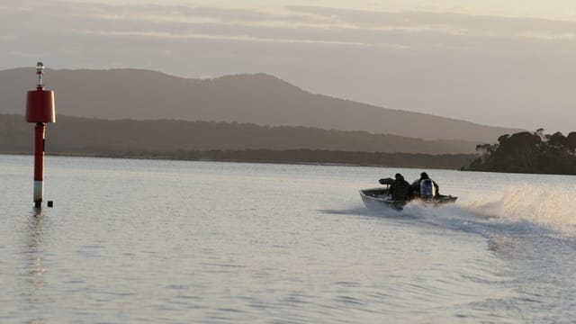 A tinny planes across glassy dawn water past the red channel marker