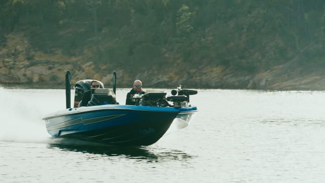 A bass boat running at speed, bow spray flying