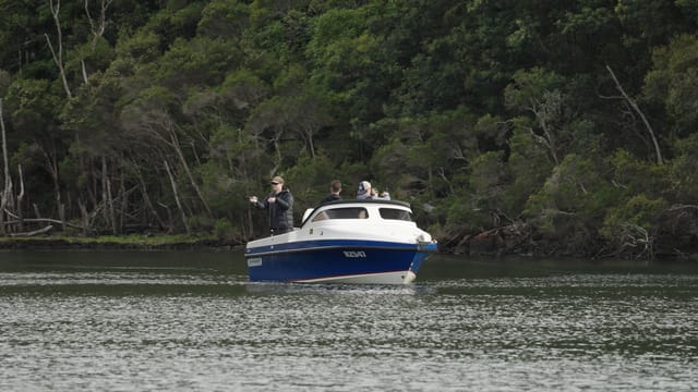 Three anglers casting from a Cootacraft tight against the bush-lined bank