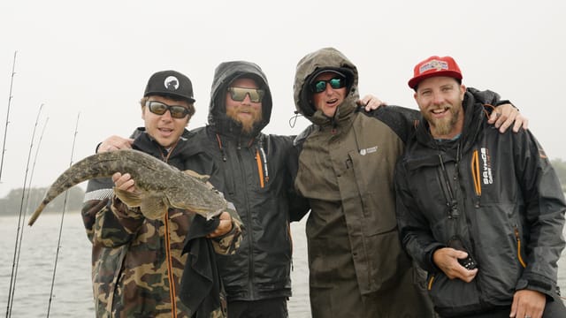 Four rain-soaked teammates arm-in-arm with a big flathead