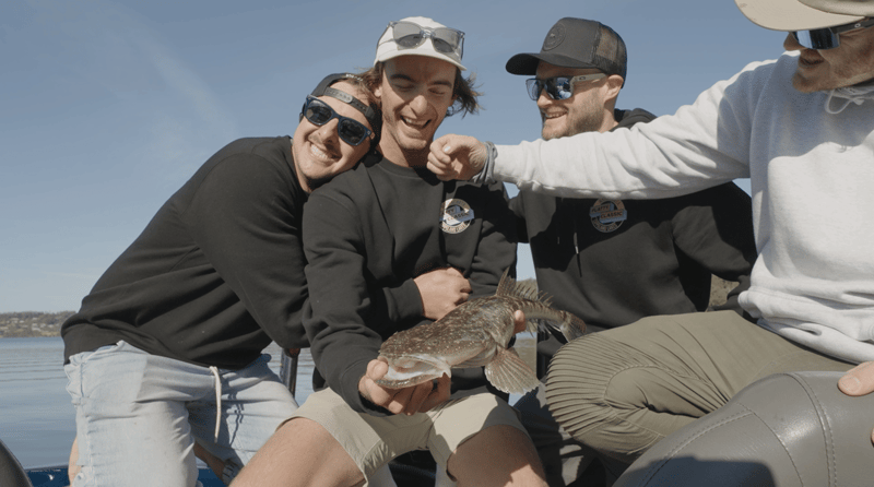 A crew of mates piled together laughing with a flathead on the boat