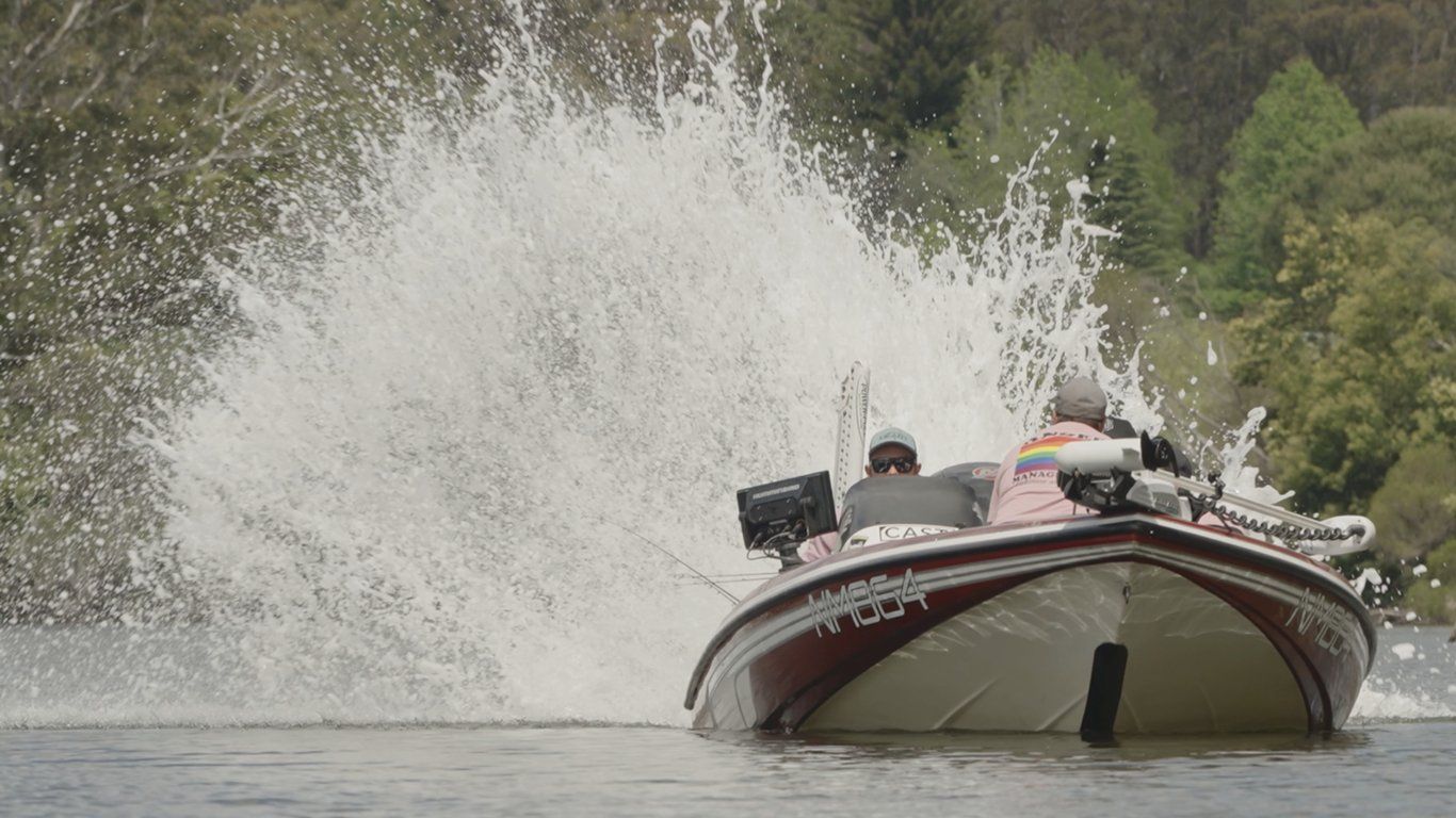 A bass boat carving across a glassy lake, throwing a towering wall of white spray