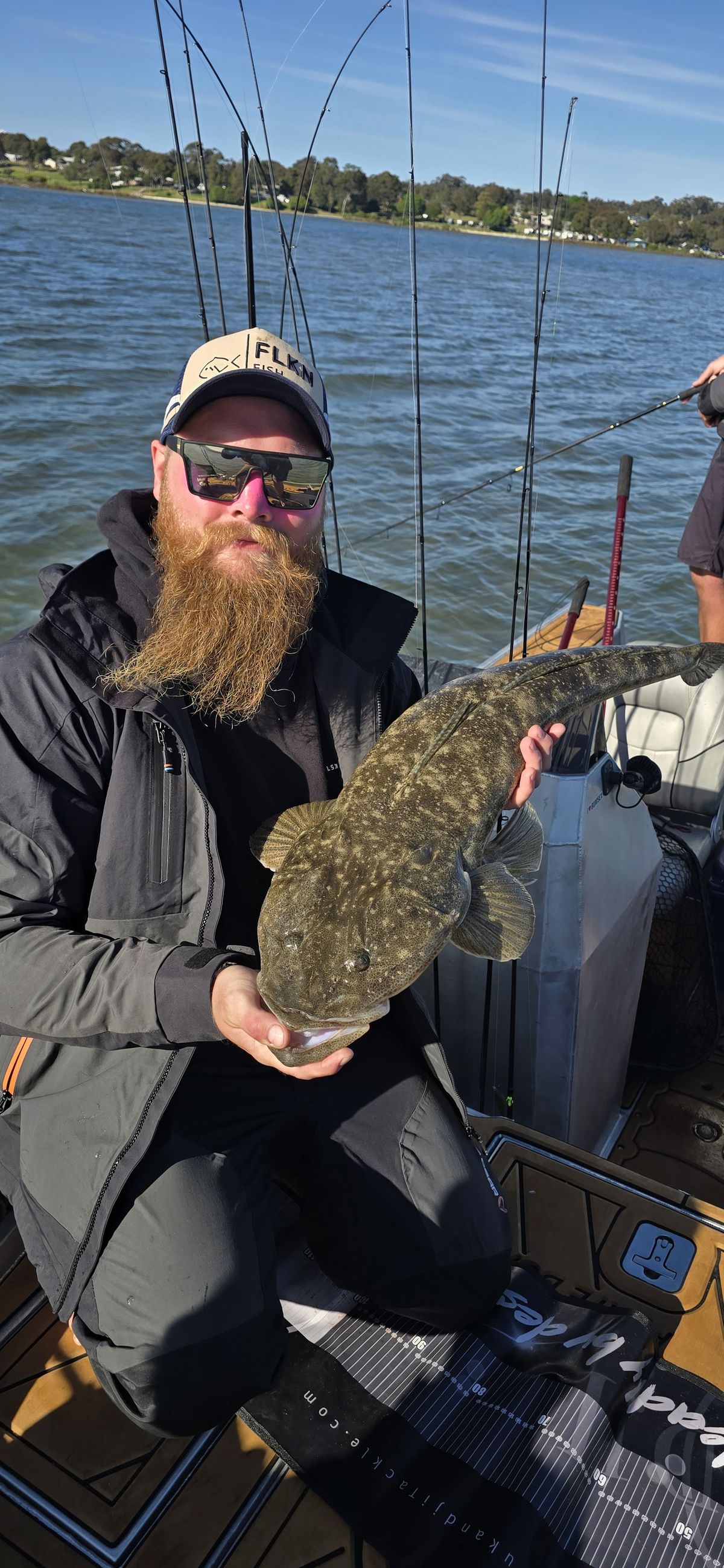 Jake holding his 90cm PB flathead on the boat, brag mat in the background