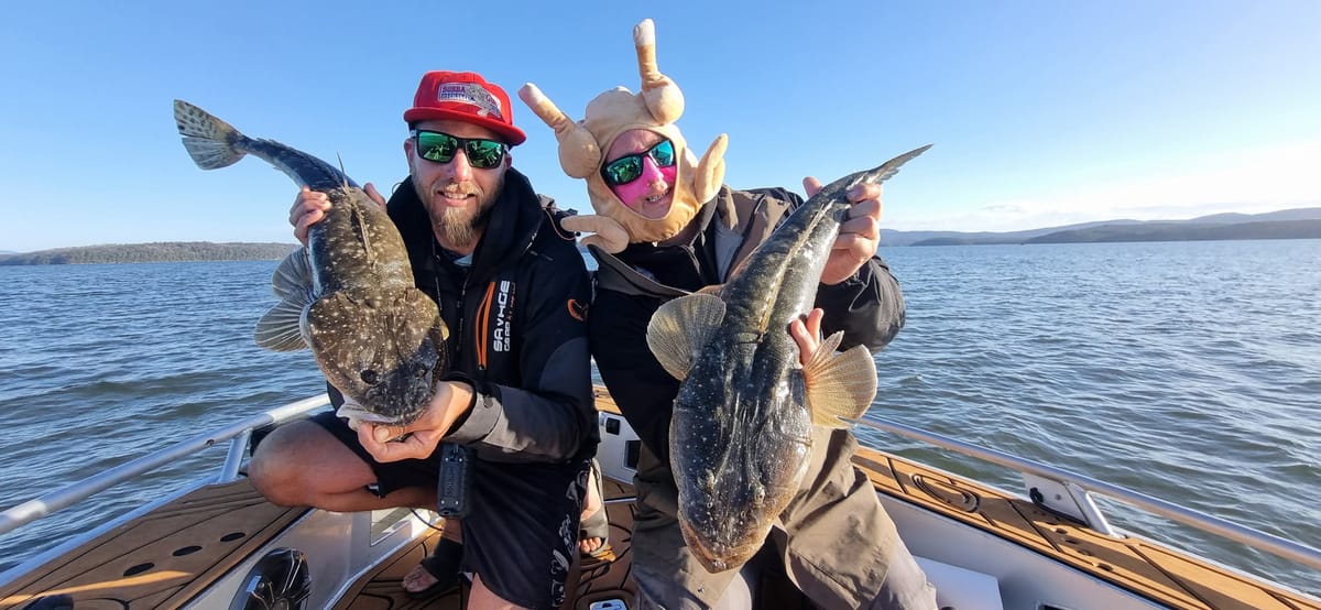 Two of the crew holding a flathead each on the boat, one wearing the chicken mask