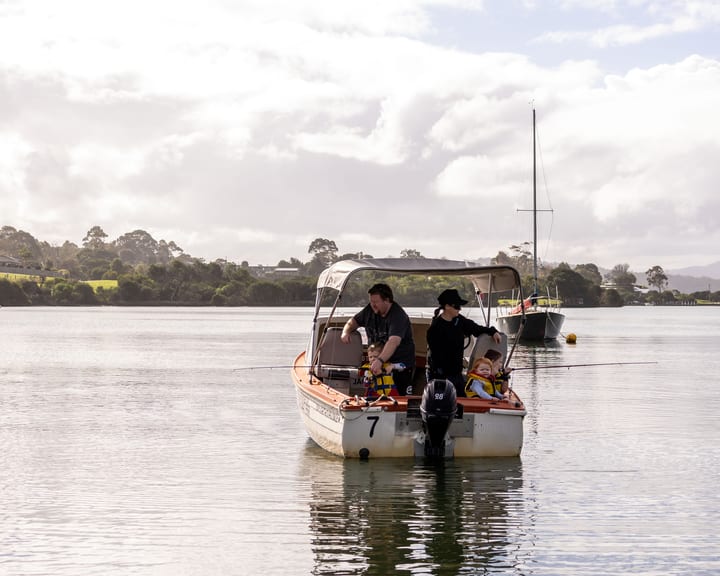 A family with toddlers in lifejackets fishing from anchored hire boat 7 on the glassy inlet