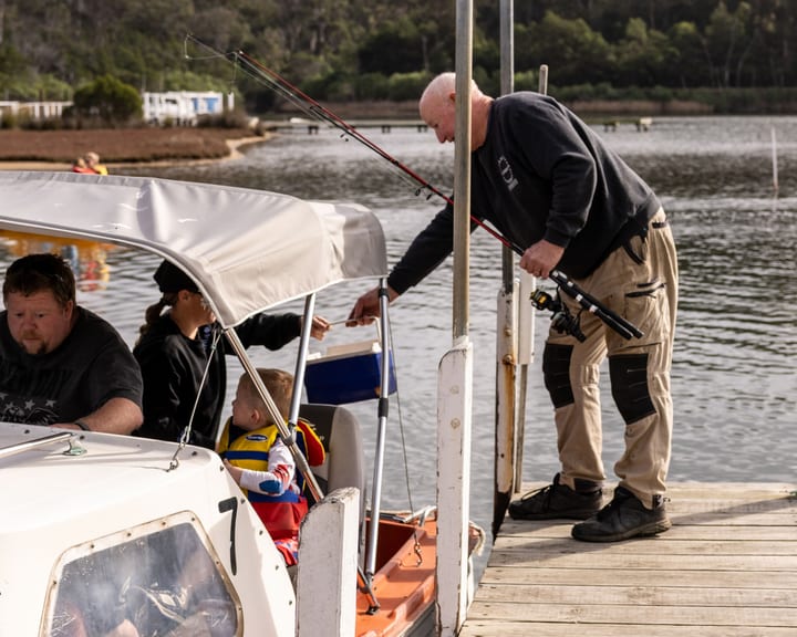 Grant leaning over the jetty passing gear to a family aboard hire boat 7
