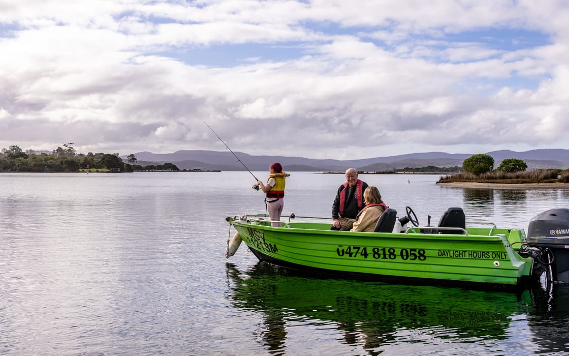 A girl casting off the bow of Kermit, the green fast boat, with her grandparents aboard and mountains across the inlet