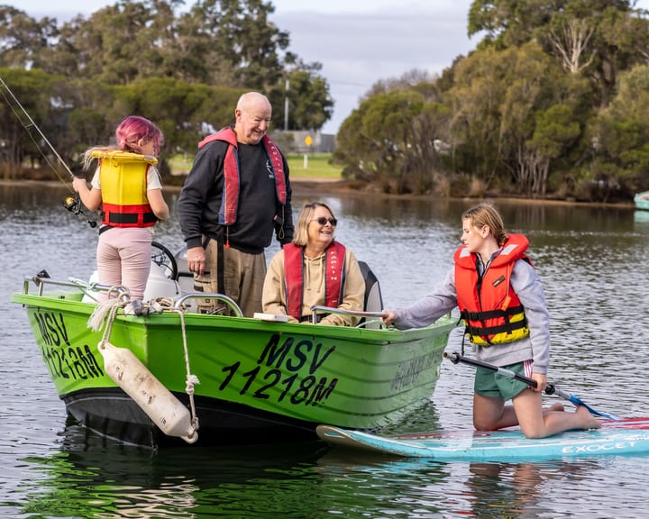 A young woman on a paddleboard chatting with a family aboard Kermit, the green fast boat