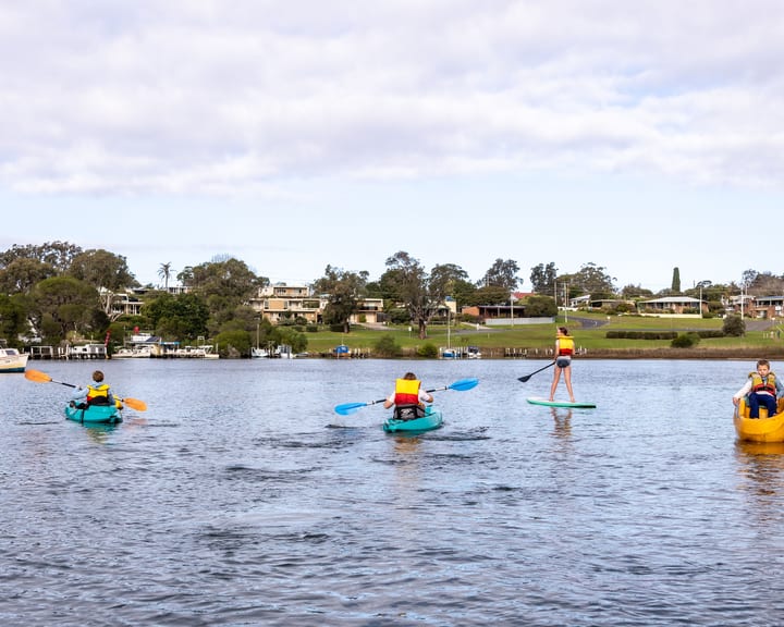 Kids on kayaks, a SUP and a pedal boat spread across the inlet