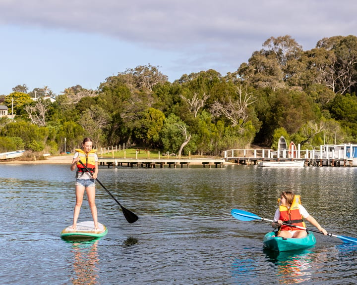 A girl standing on a SUP and a kayaker in lifejackets with jetties along the far shore