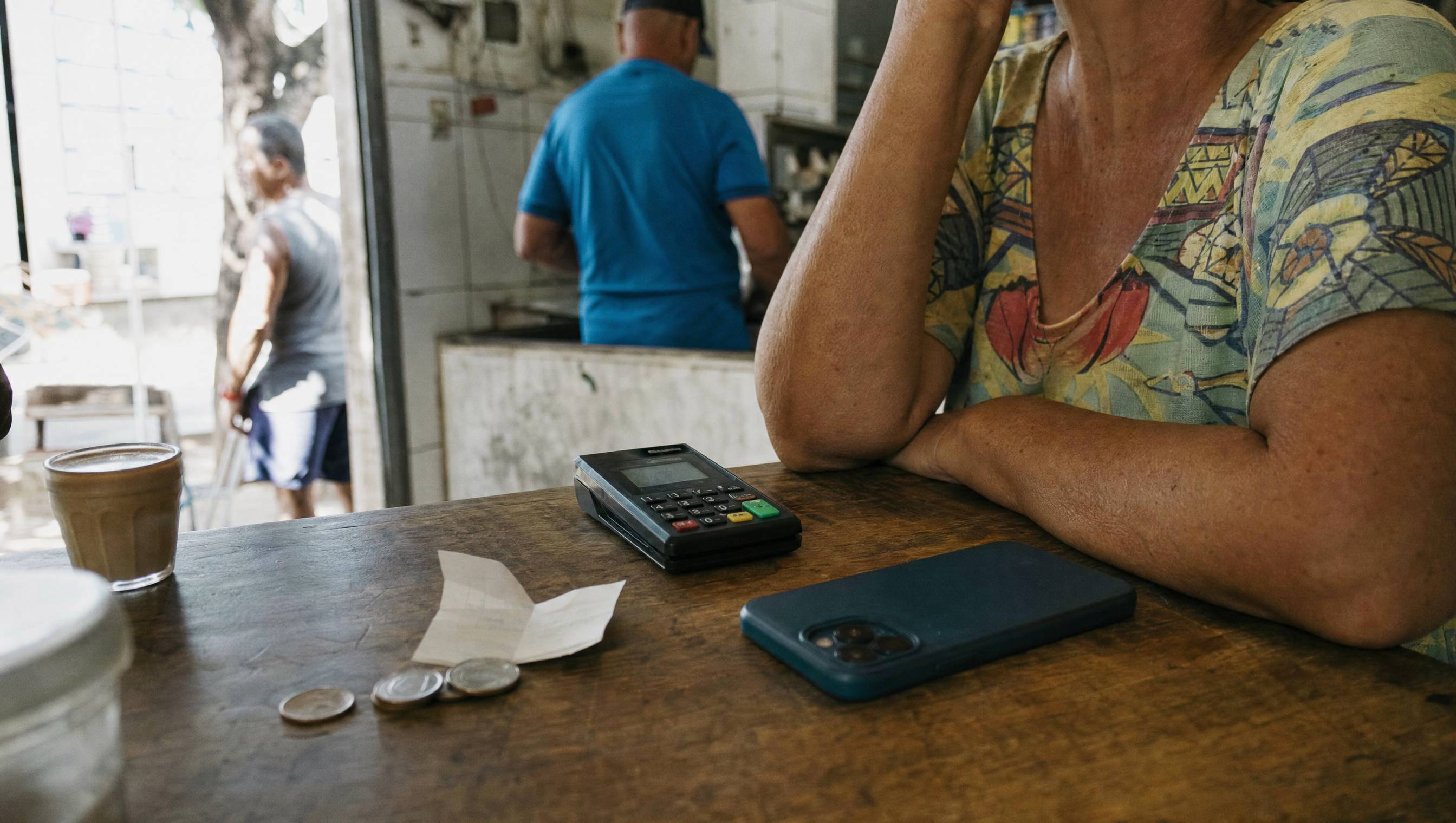 Maquininha, moedas e um comprovante no balcão de um bar