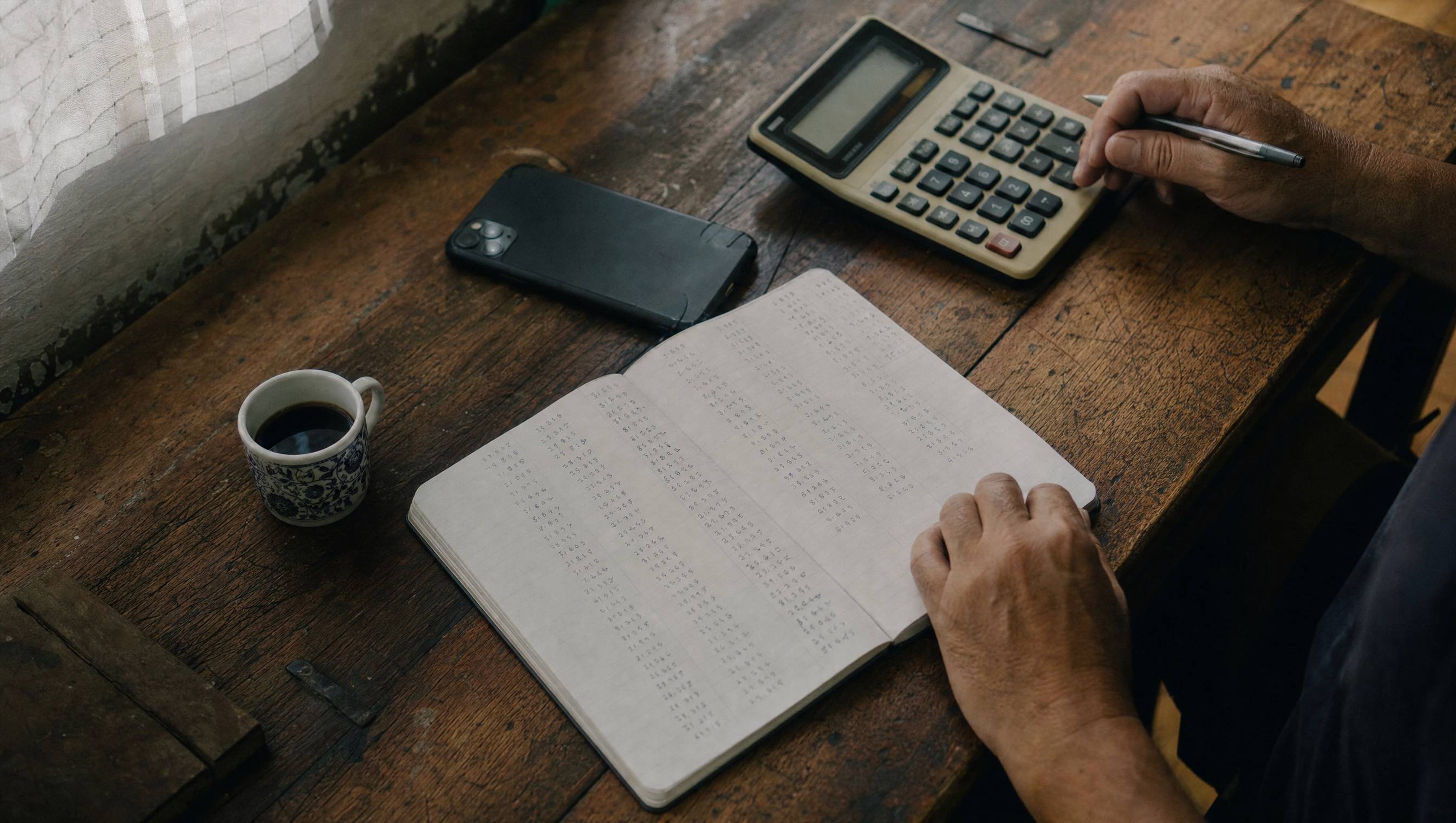 Caderno com colunas de números, calculadora de mesa e café