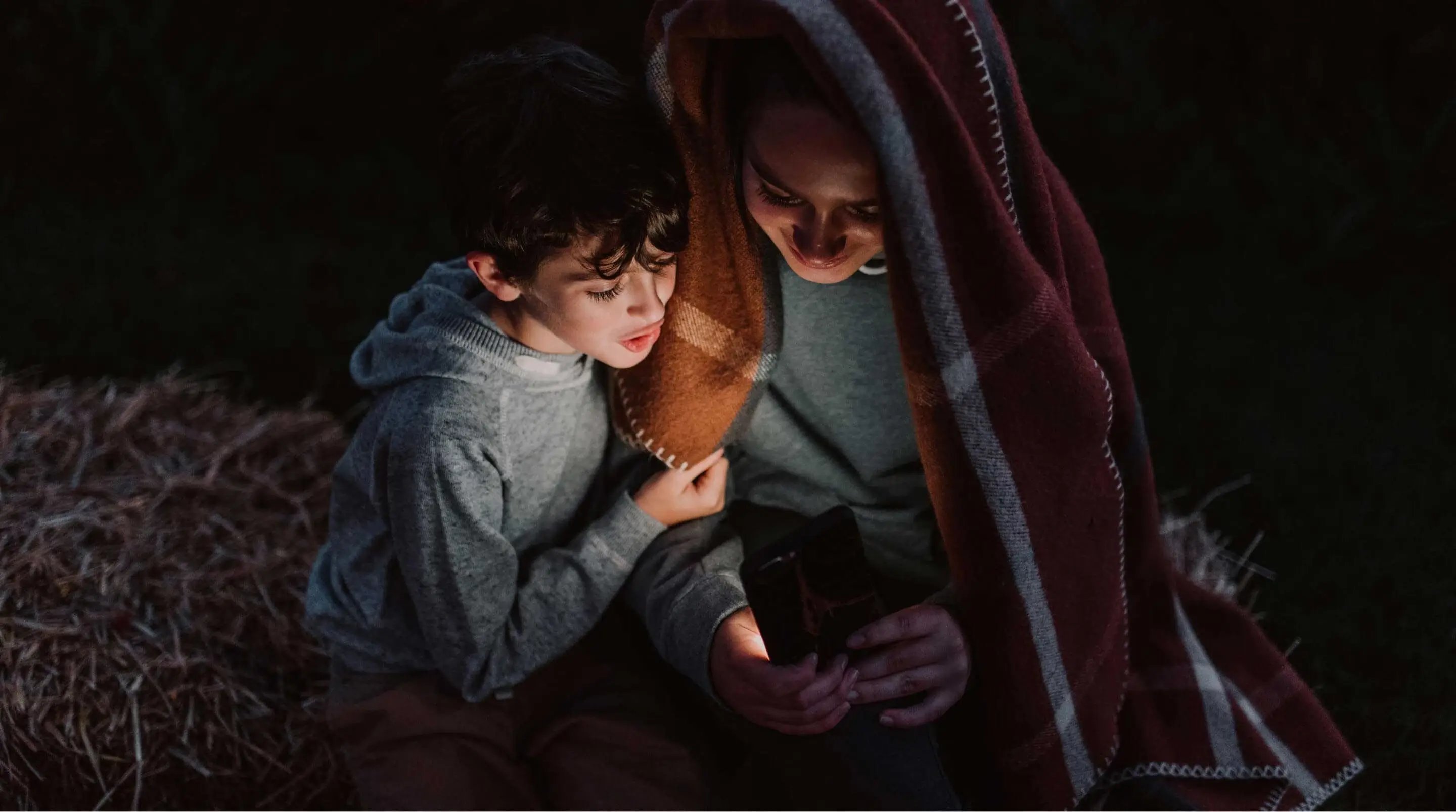 Mum and son looking at a glowing phone screen while camping