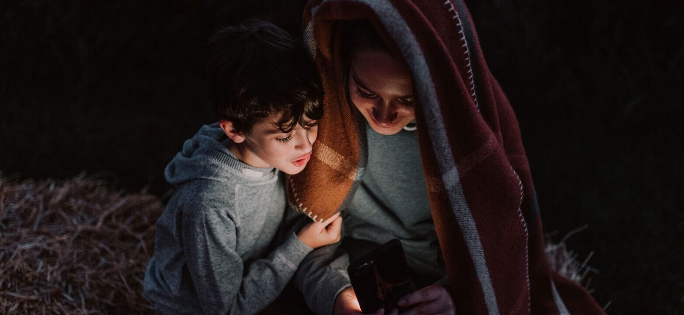 Image of a woman and a child looking at a glowing device screen at night