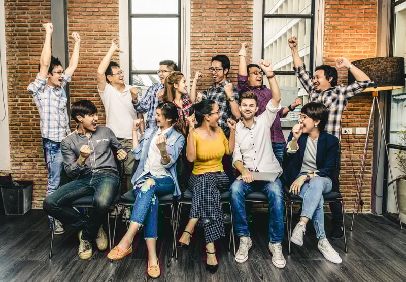 A joyful and energetic team celebrating success together with smiles, cheers, and raised arms.