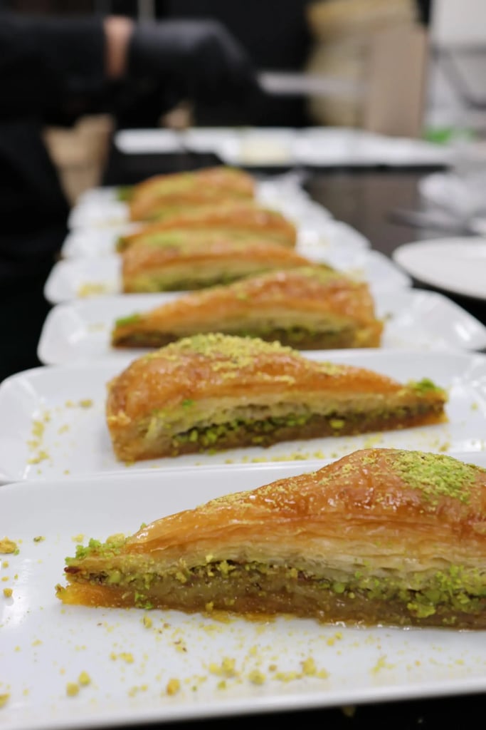 Baklava slices topped with crushed pistachios, served on white rectangular plates in a row