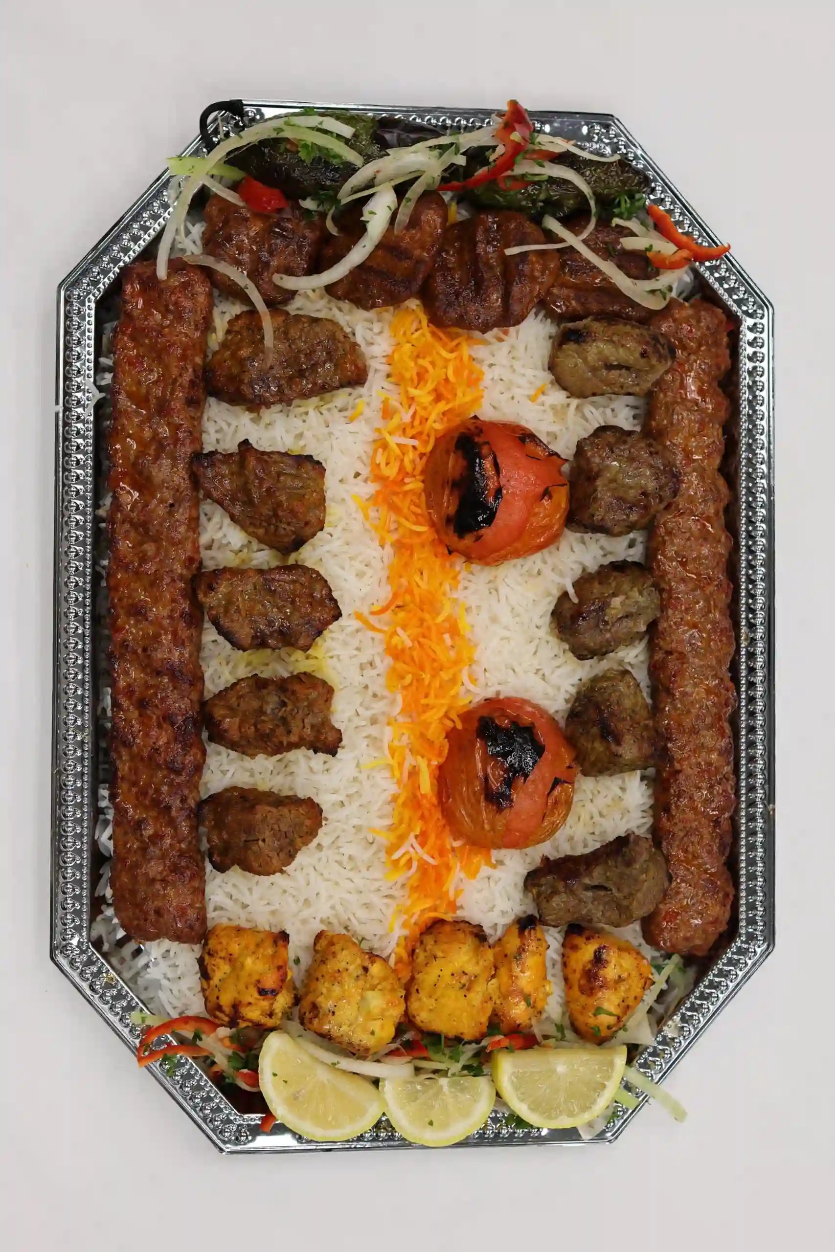 Mixed grill platter with koobideh, chicken, beef, grilled tomato, and saffron rice, garnished with vegetables and lemon slices