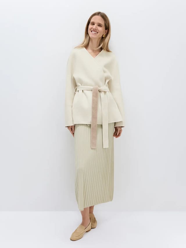 Model wearing an off-white wool lyocell belted coat with a V-neck, wrap front, and self-tie belt.