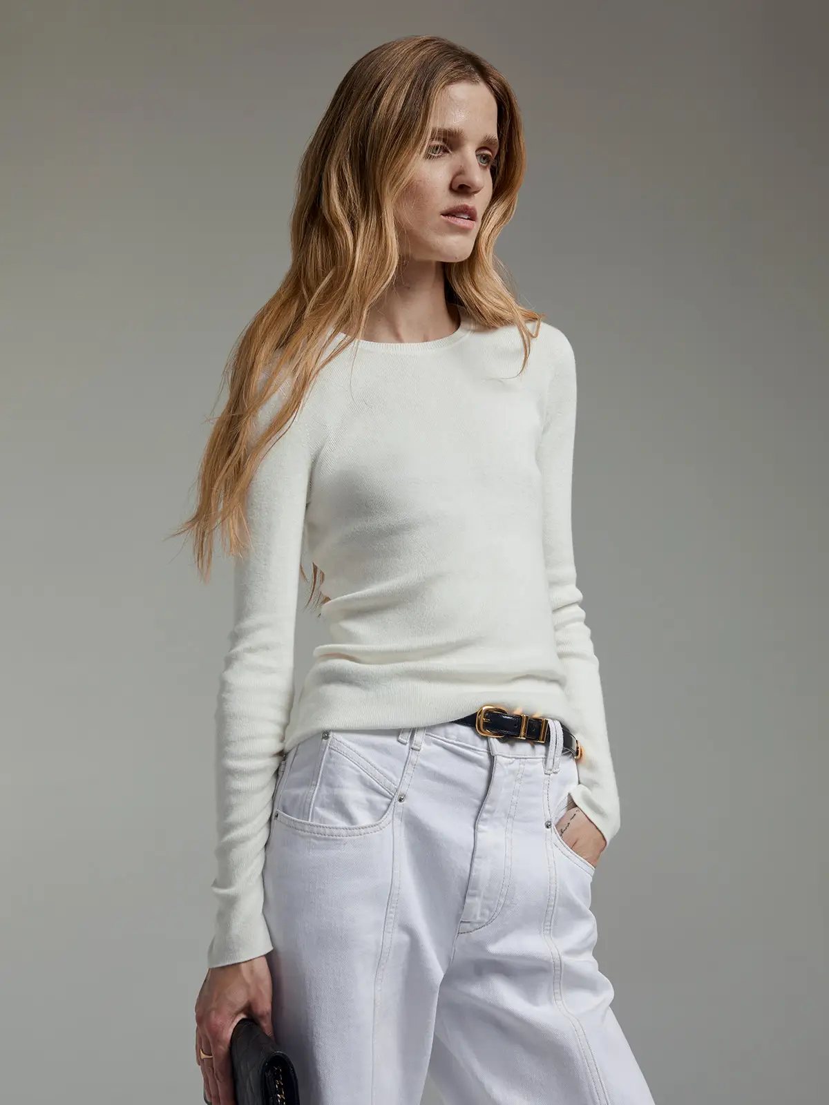 Model in a white slim fit long-sleeve knit top with crew neck, paired with white pants and a belt.