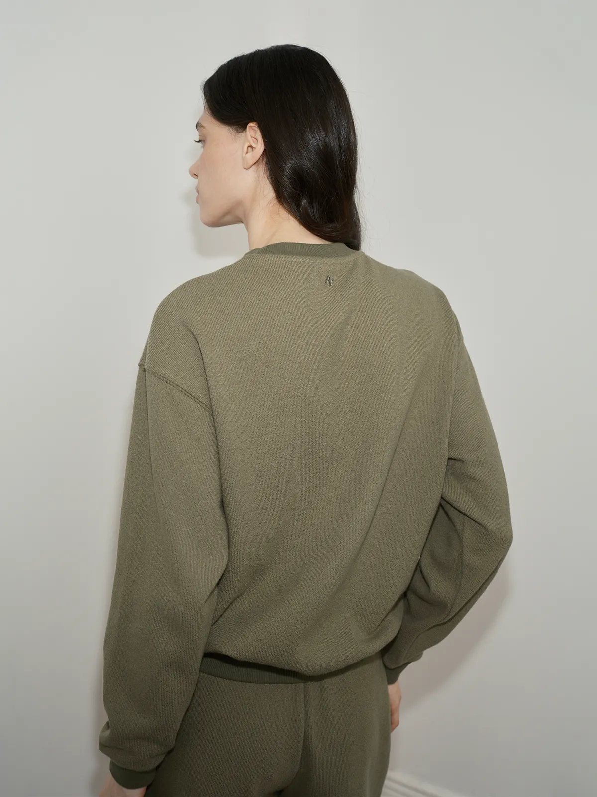 Back view of model in olive green SOREN sweatshirt showing subtle 'A' logo at nape and seam lines