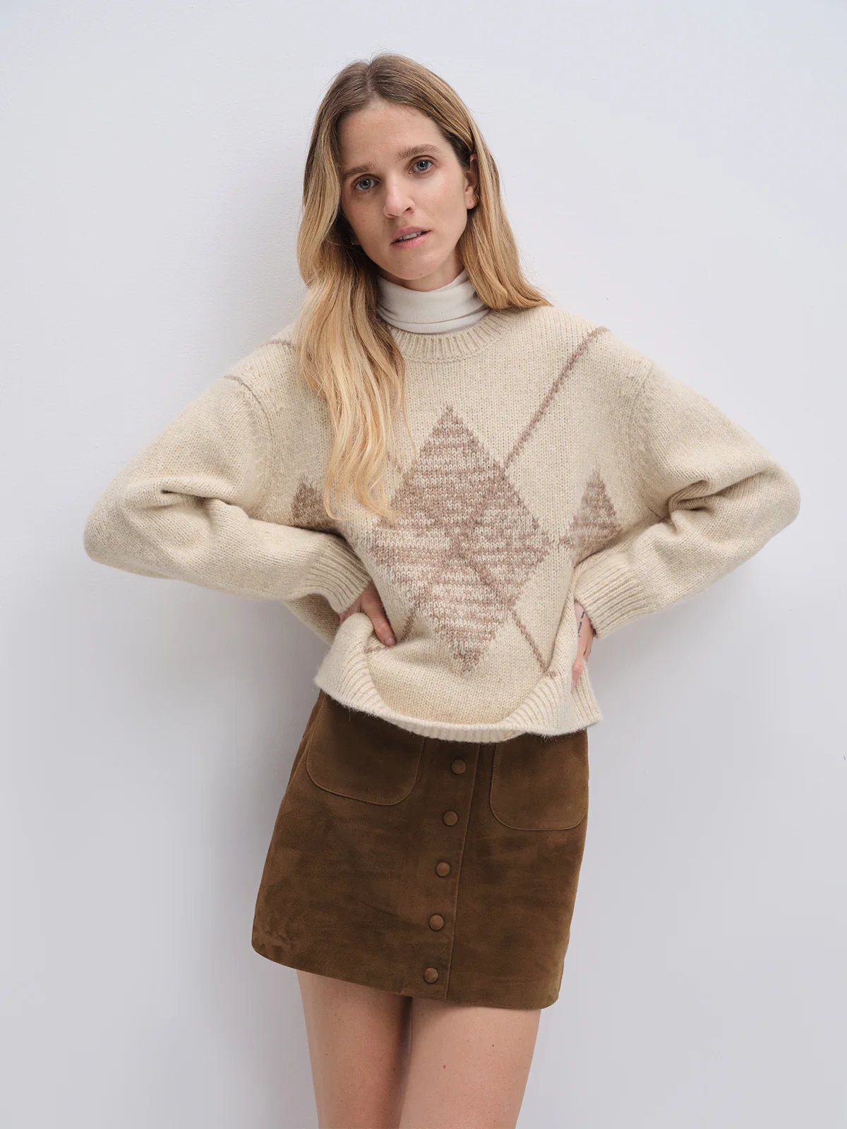 Model in the Oatmeal PHOEBE jacquard jumper featuring a diamond design, worn with wide-leg trousers and loafers, clutch held at hip.