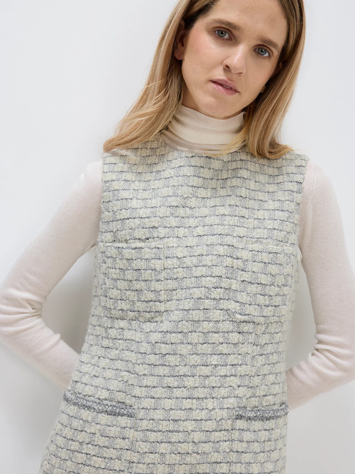 Close-up of andreatang light grey bouclé check sleeveless dress layered over an ivory turtleneck
