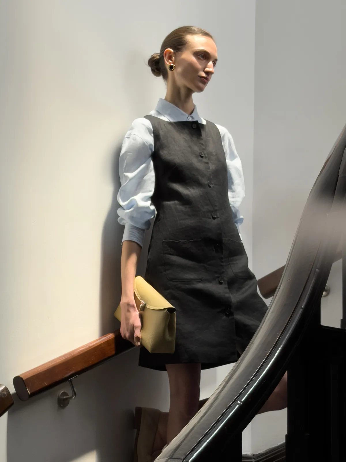 Model wearing black MARISA dress layered over light blue shirt on staircase