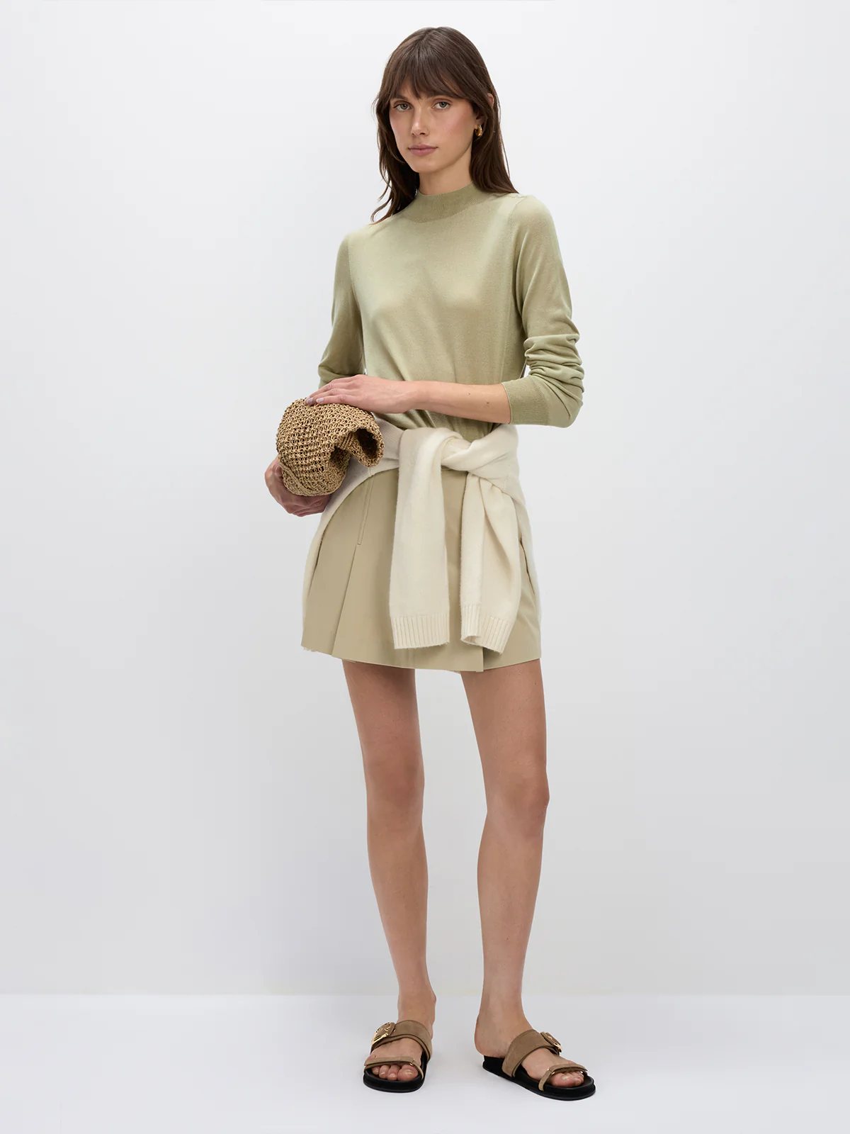 Side view of a model in a brown silk lyocell mock-neck top with long sleeves, tucked into dark trousers with a brown belt and buckle.