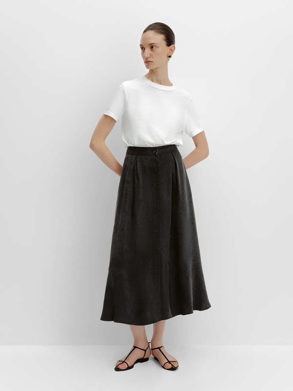 Front full view of black NOBU Midi Skirt with white crew-neck tee and hands on hips