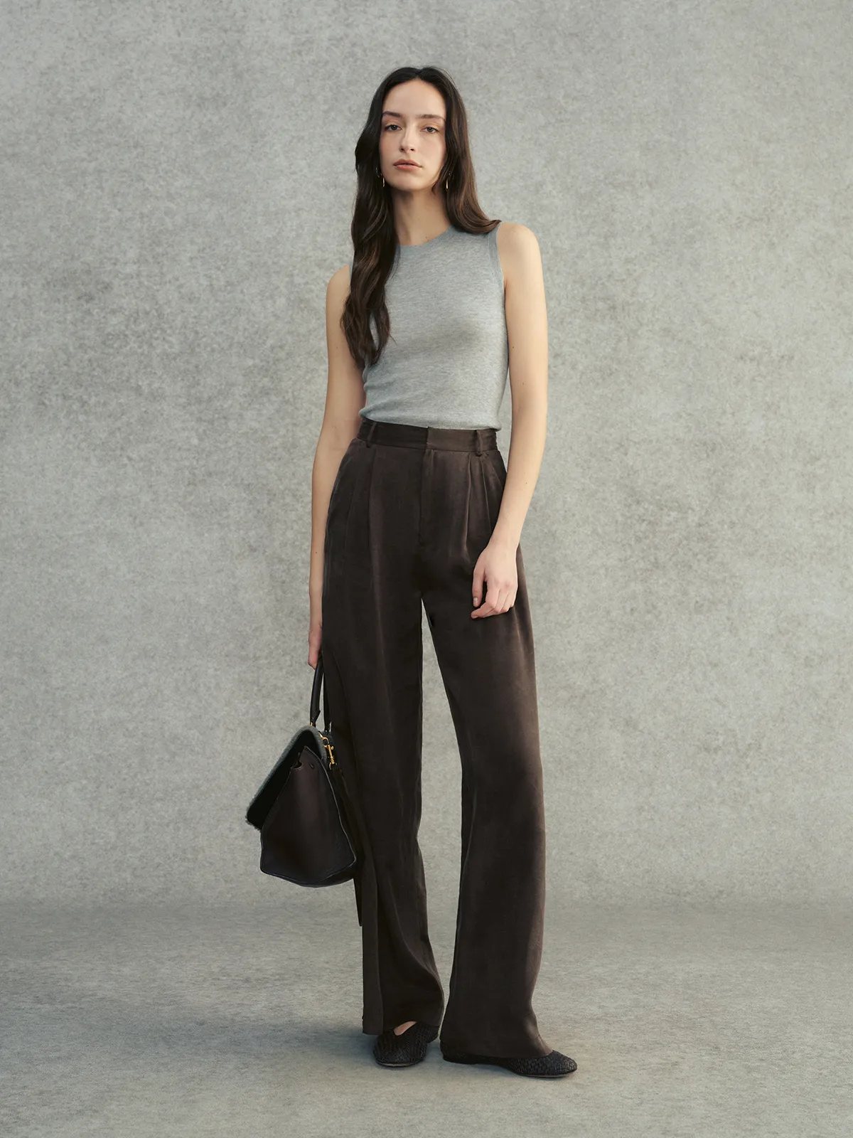 Model wearing DELIA sleeveless knit top in cloud grey with chocolate brown wide-leg trousers and black leather tote