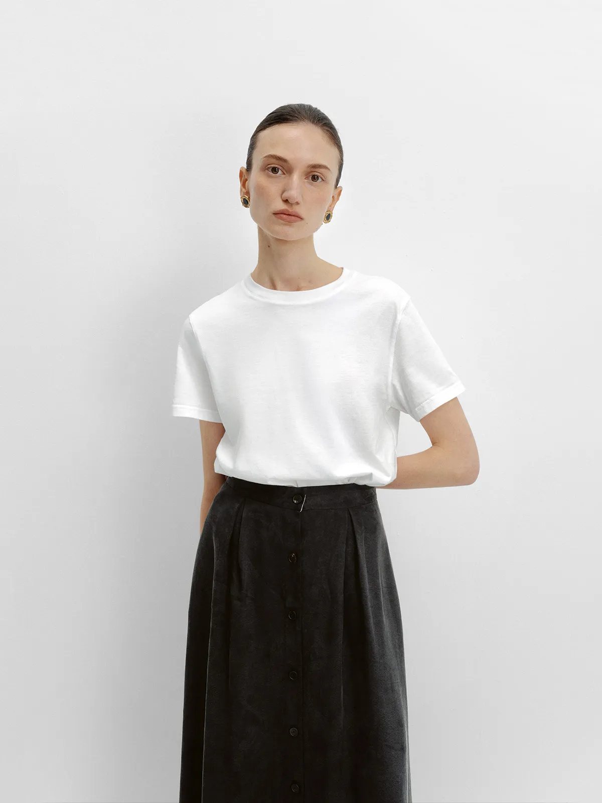 Model wearing white relaxed-fit crewneck t-shirt with black high-waisted button-front skirt, minimalist Parisian chic styling by andreatang