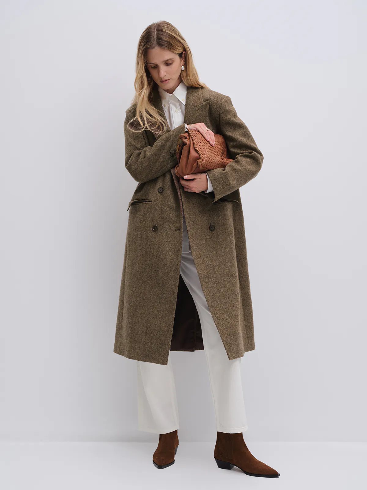 Model holding a woven clutch, wearing a brown wool and alpaca tweed long coat with a contrasting dark collar.