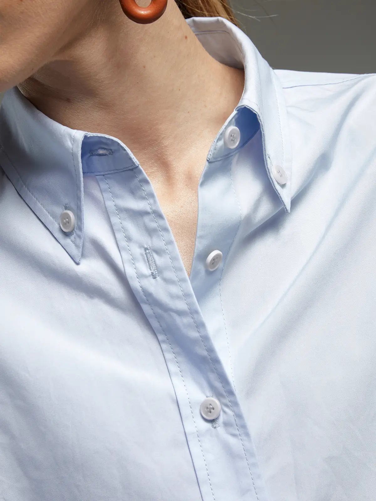 Close-up of the collar and button placket of a light blue oversized Pima cotton shirt, showing stitching and fabric texture.