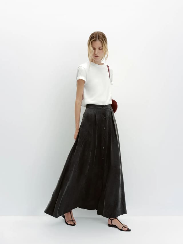 Model with blonde hair wearing white relaxed t-shirt, black velvet maxi skirt, and brown leather sandals for elevated evening look