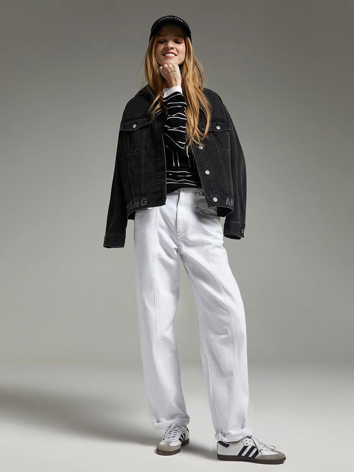 andreatang washed-black denim jacket with logo hem worn over striped top, white jeans, cap and sneakers