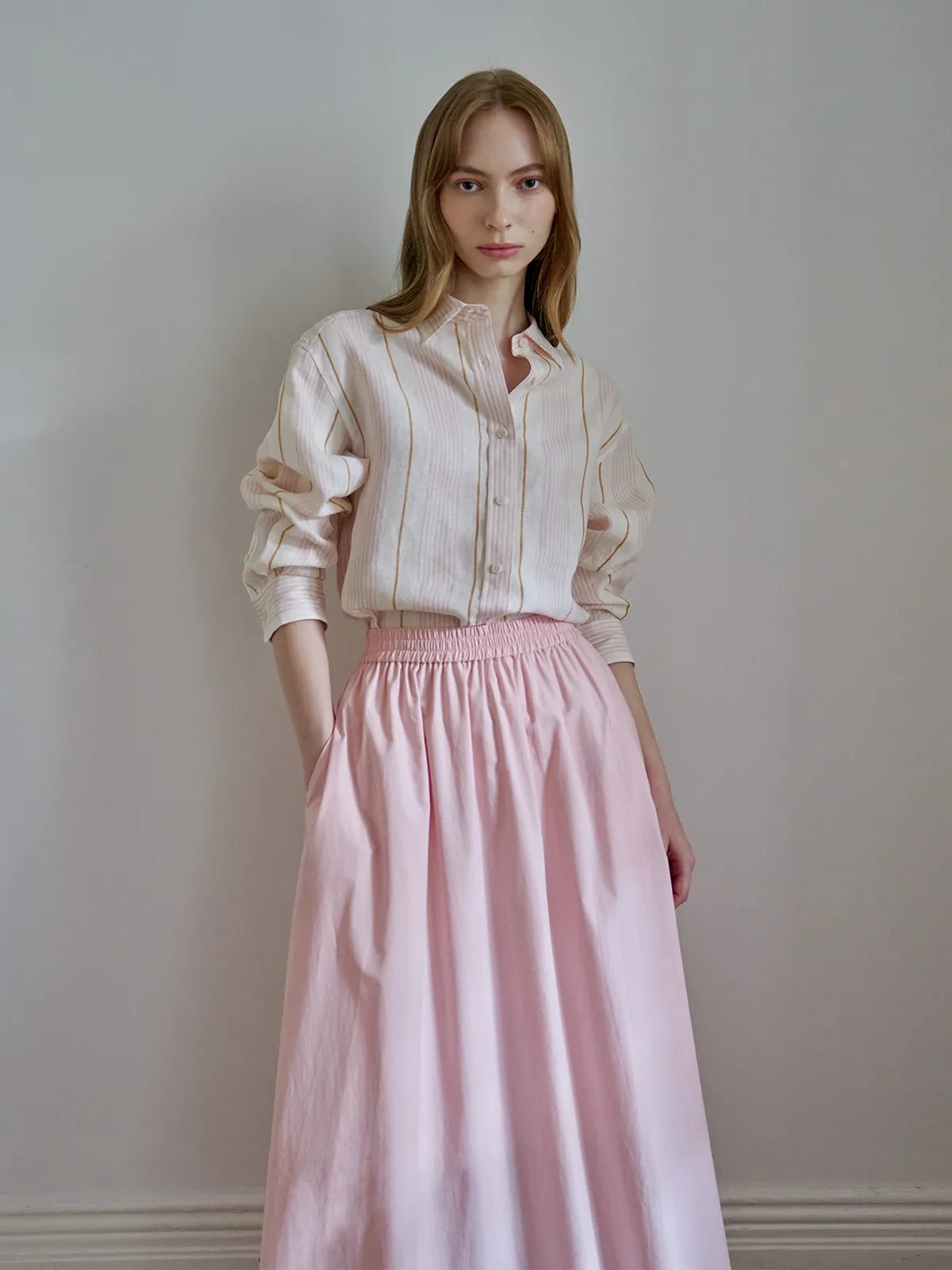 Model wearing MYRA linen shirt with pink midi skirt, minimalist studio look