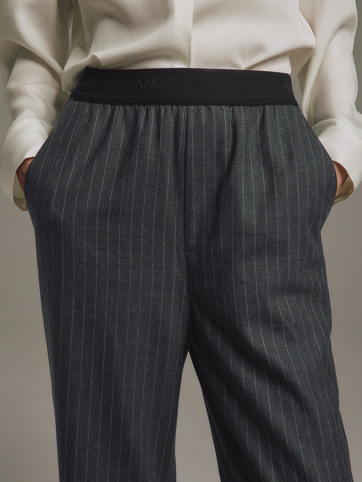 Side view of Black/White wool-blend straight trousers with elastic waist, worn with a long-sleeve top and dark woven slippers.