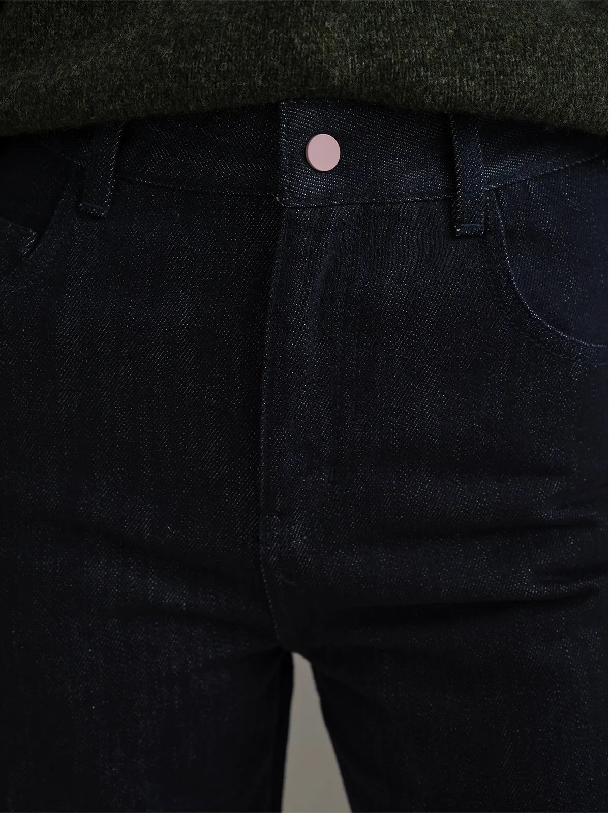 Top-down close-up of blush pink button at waistband with olive sweater hem overlay